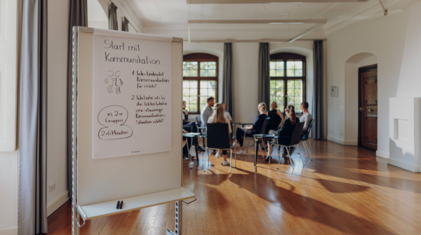 Flipchart mit Aufgabe und Seminargruppe im Hintergrund